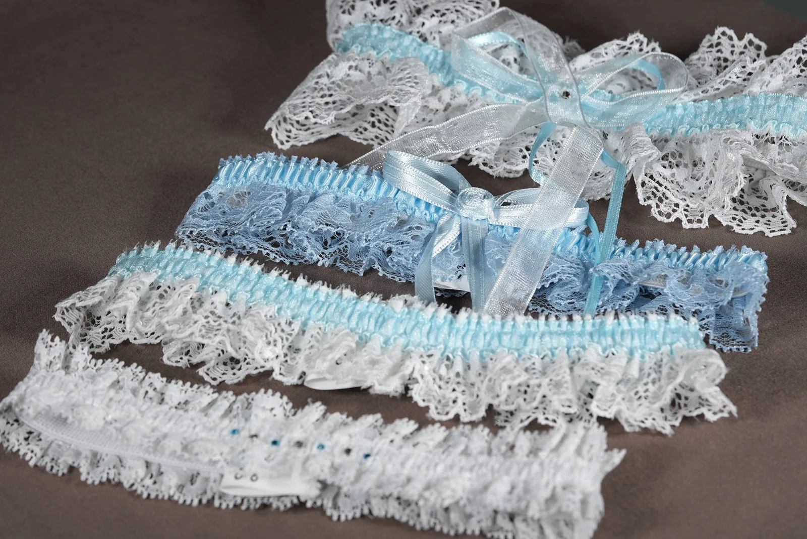 Strumpfbänder von Bianco Evento in vier verschiedenen Modellen – elastische Braut-Strumpfbänder in Universalgröße aus Spitze und Tüll in Ivory und Blau mit eleganten Verzierungen.